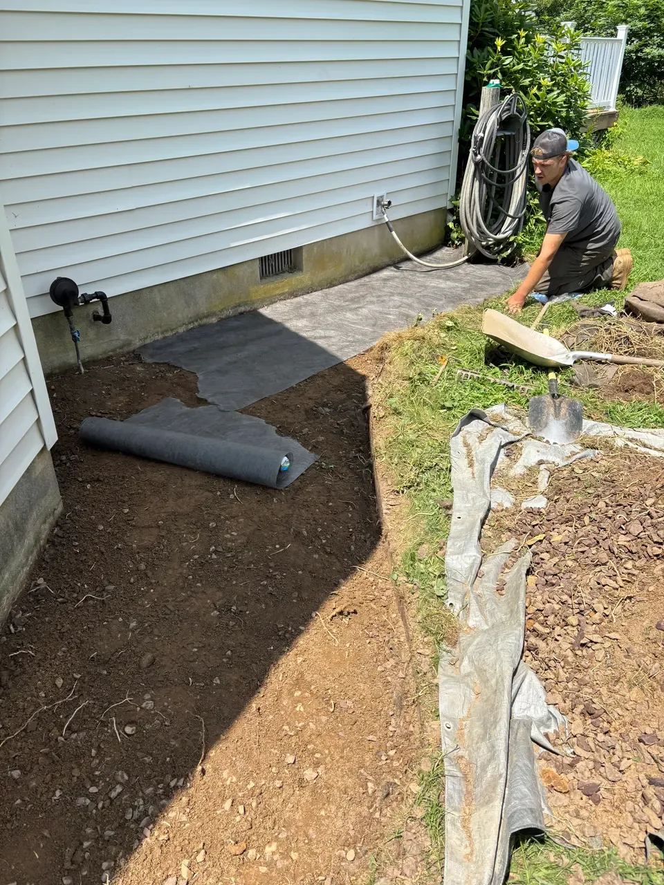 Crew member preparing a garden bed and laying landscape fabric beside a house