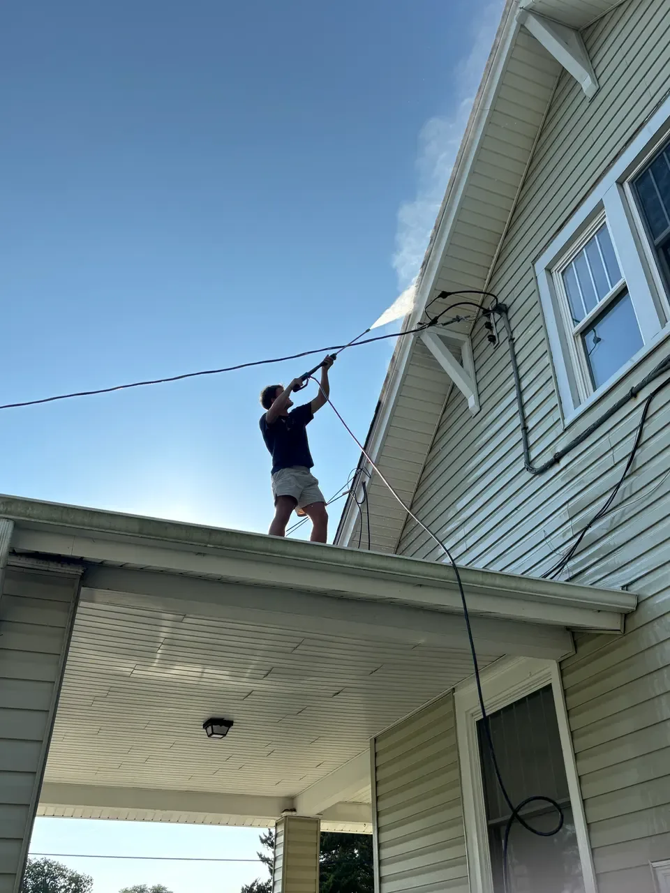 Crew member washing upper-story siding beneath the eaves